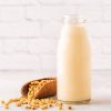 A bottle of soy milk and soy beans on a light background.