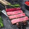 Rare Ahi tuna steak slices on a meat cleaver. Black background. Top view.