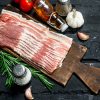 Raw bacon with rosemary branches. On black rustic background.