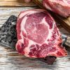 Fresh raw beef striploin steak, chicken breast fillet, pork and salmon steak. White wooden background. Top view. Copy space.