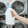 Holding bottle with detergent with professional machines on the background at the laundry