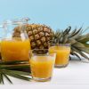glass and pitcher of pineapple juice and whole fruit on blue background