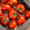 Ripe Red tomatoes in wooden market box. Wooden background. Top view.