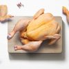 Whole chicken on a flat lay of a kitchen with chicken pieces from above