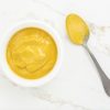 Mustard sauce in a bowl and spoon on white marble table. Top view